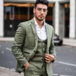 Elegant businessman in a green suit posing confidently on a city street with an urban background.