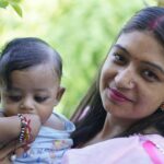 A loving mother holding her baby outdoors, showcasing happiness and cultural attire in a summer setting.