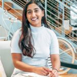 A smiling woman sitting indoors, exuding warmth and confidence.
